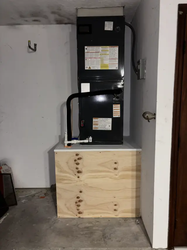 Replacement air handler installed on a new plywood platform with a sheet-metal top, clean PVC condensate drain with a safety switch, and an insulated refrigerant line set.