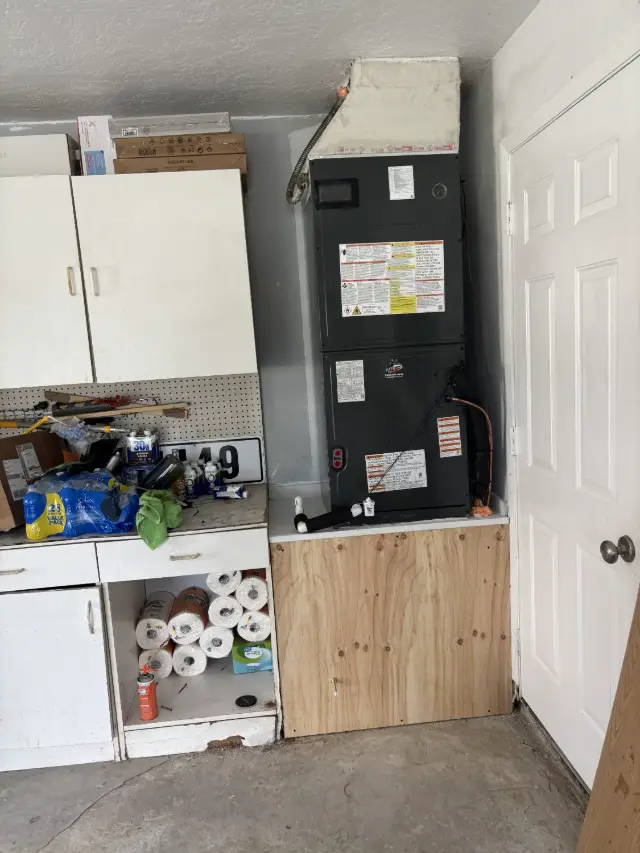 Air handler installed in a garage alcove on a plywood stand, with an insulated supply plenum above and an Ox Air and Heat service sticker on the cabinet.