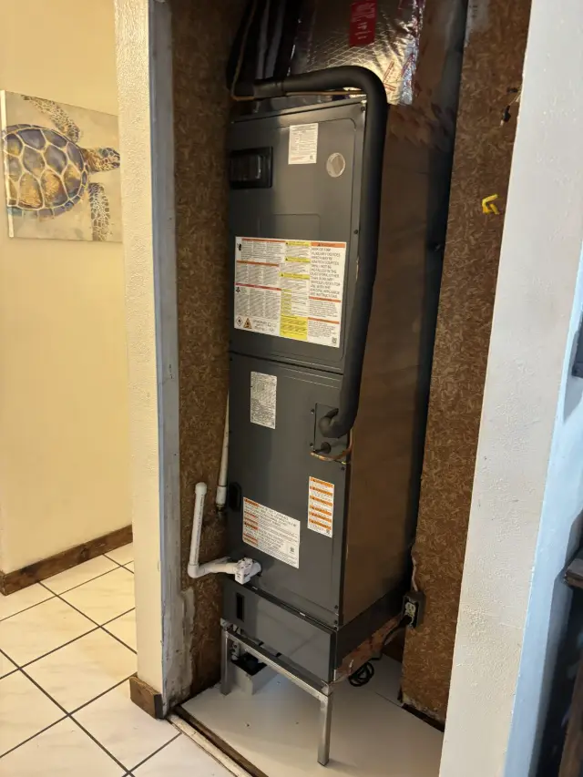 Air handler installed in a narrow interior closet with the refrigerant line set routed overhead and a PVC condensate drain with a safety float switch.