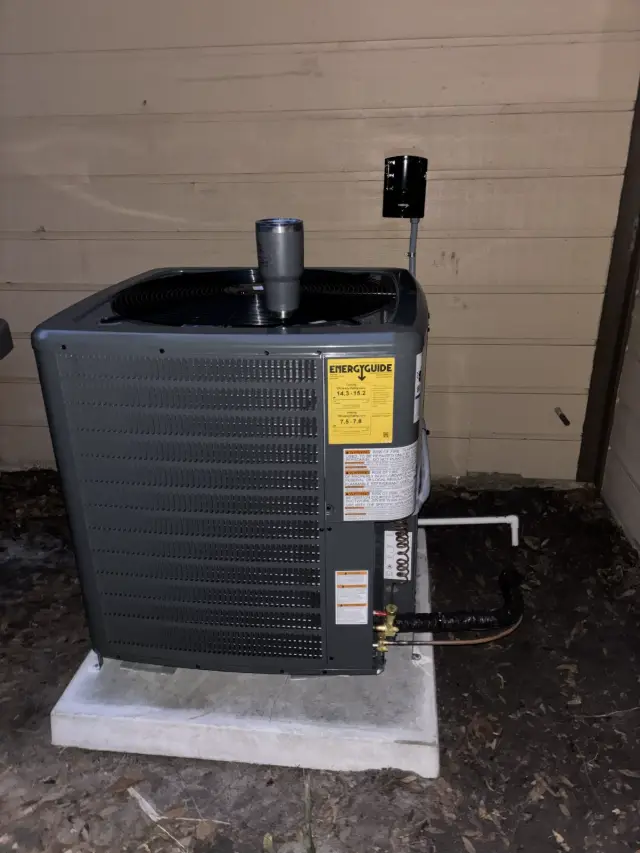Close view of a newly installed Goodman condenser showing the yellow EnergyGuide label, brazed copper line set, and service valves.