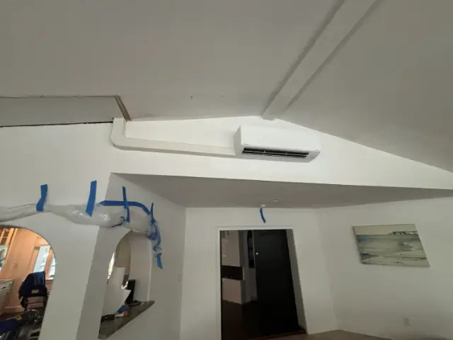 Daikin wall-mounted mini-split indoor head installed high on an interior wall with a painted line-set cover running to the ceiling.